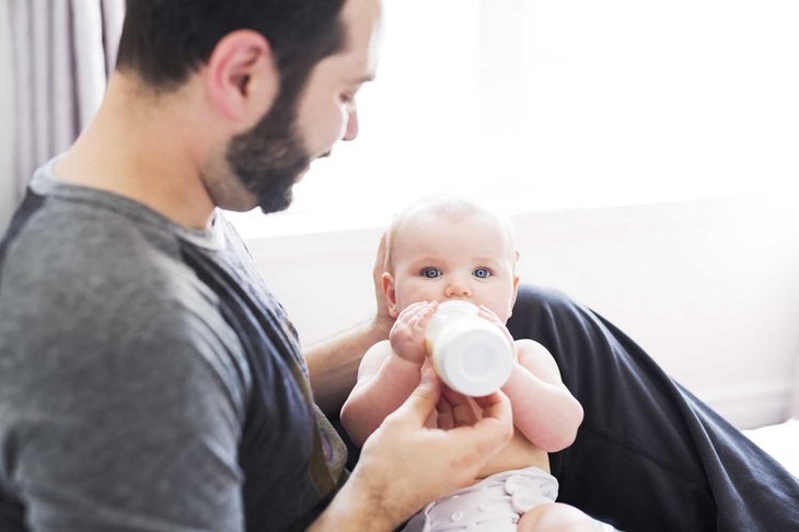 A Happy man feeding milk to baby girl at home