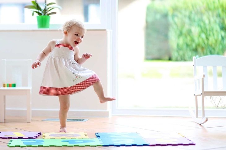 Funny toddler girl dancing indoors. Little child having fun moving and jumping in a sunny white room at home or kindergarten